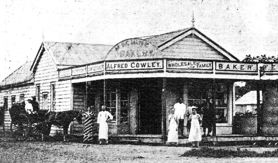 Alfred Cowley's shopfront in Nuku'alofa, its painted fascia reading Alfred Cowley, Wholesale and Family Baker, with staff in white aprons and a horse and cart loading at the side.