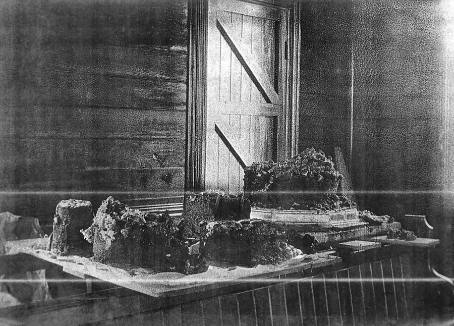 The wedding cake broken apart after its voyage, laid out on boards in a timber-walled room.