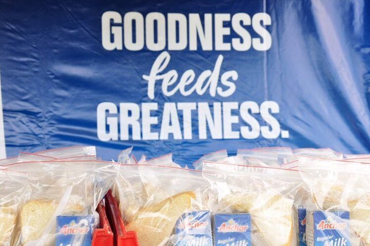 Packed school lunches of sandwiches and Anchor milk, lined up beneath a Goodness Feeds Greatness banner.