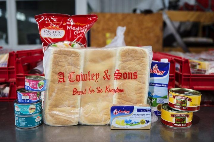 A family food pack laid out: A. Cowley & Sons bread, Anchor milk and butter, rice, tinned tuna and corned beef.