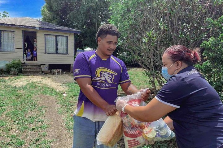 A food parcel delivered to a family at their home, children watching from the doorway.