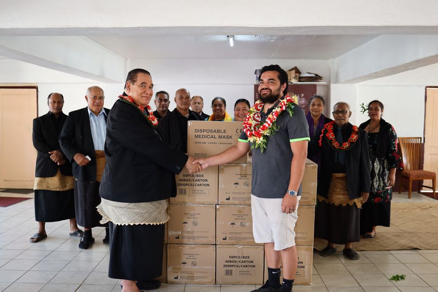 The handover inside the hall, the congregation gathered behind the stacked cartons.