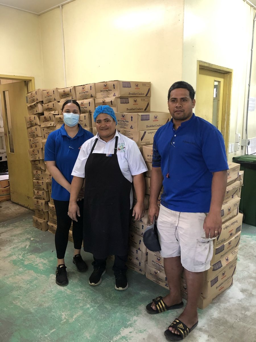 Kitchen staff and ACS beside the stacked cartons in the kitchen store.