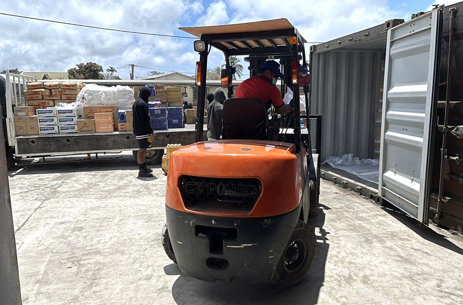 A forklift moving palletised stock between a container and waiting delivery trucks in the ACS yard.