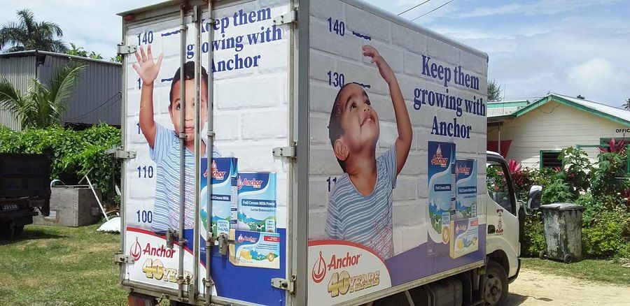 An ACS delivery truck in Anchor livery, Keep them growing with Anchor across the back and the side, parked on a village roadside.