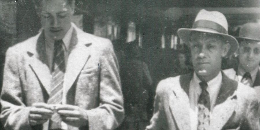 Frank Cowley walking beside his father Francis, both in light suits, on a city street.