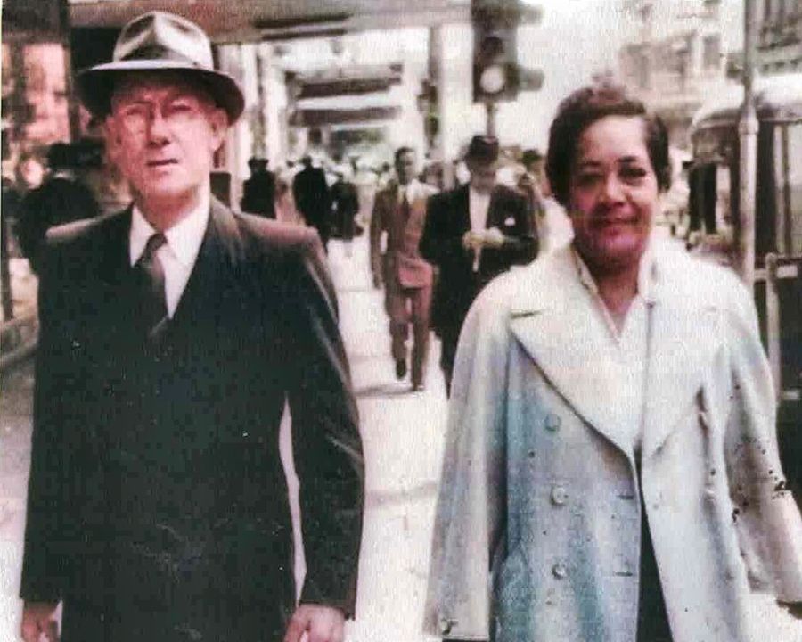 Francis and Vangana Cowley walking together in the city, he in a suit and hat, she in a pale coat.