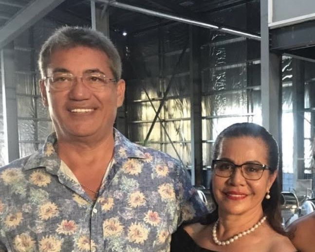 Alfred and Atiū Cowley together, smiling, he in a floral shirt and she in black with a pearl necklace.