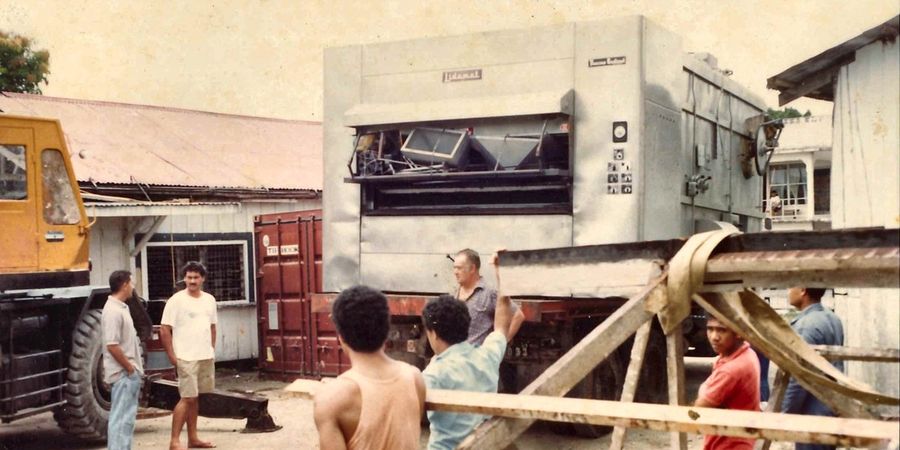A new bakery oven arriving on a flatbed truck, with a crane alongside and staff gathered to unload it.