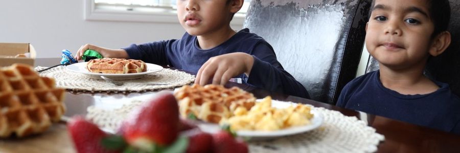 Two boys at the table with waffles, scrambled eggs and strawberries.