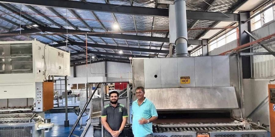 Alfred and Francis Cowley standing beside the tunnel oven on the plant floor.