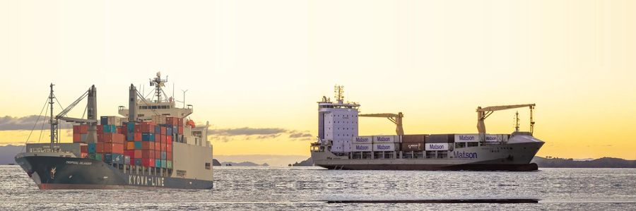 A Kyowa Line vessel and a Matson vessel under way at sunset among Pacific islands.