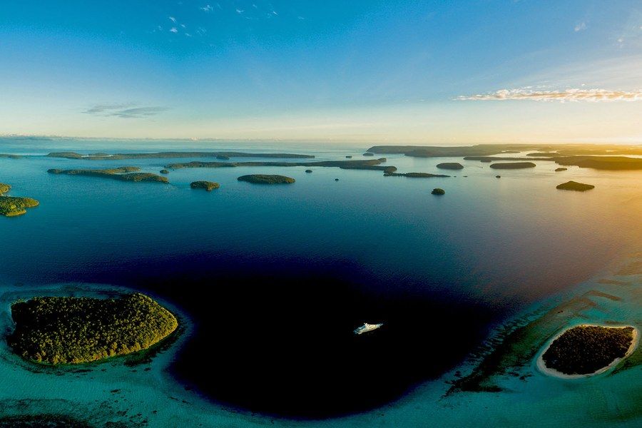 Aerial view of the Tongan islands at sunrise, with a vessel anchored in a deep blue channel between reefs.