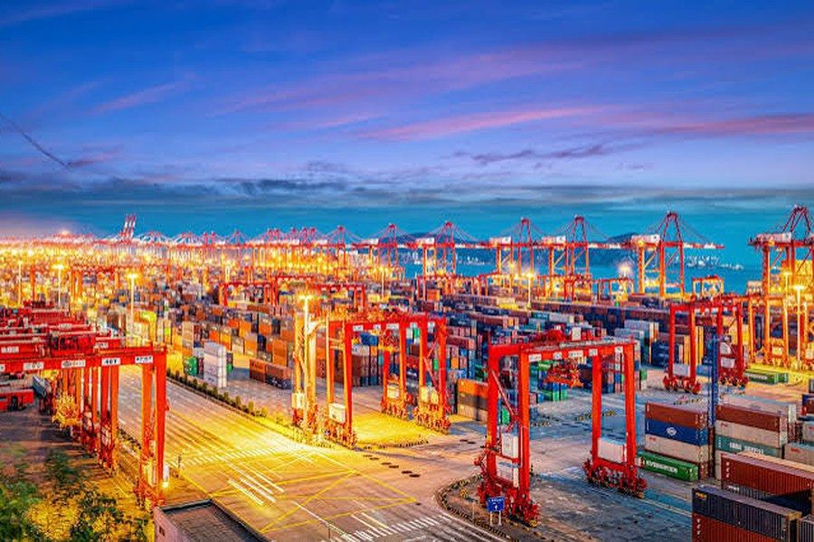 A container terminal in China lit at dusk, with gantry cranes and stacked containers.