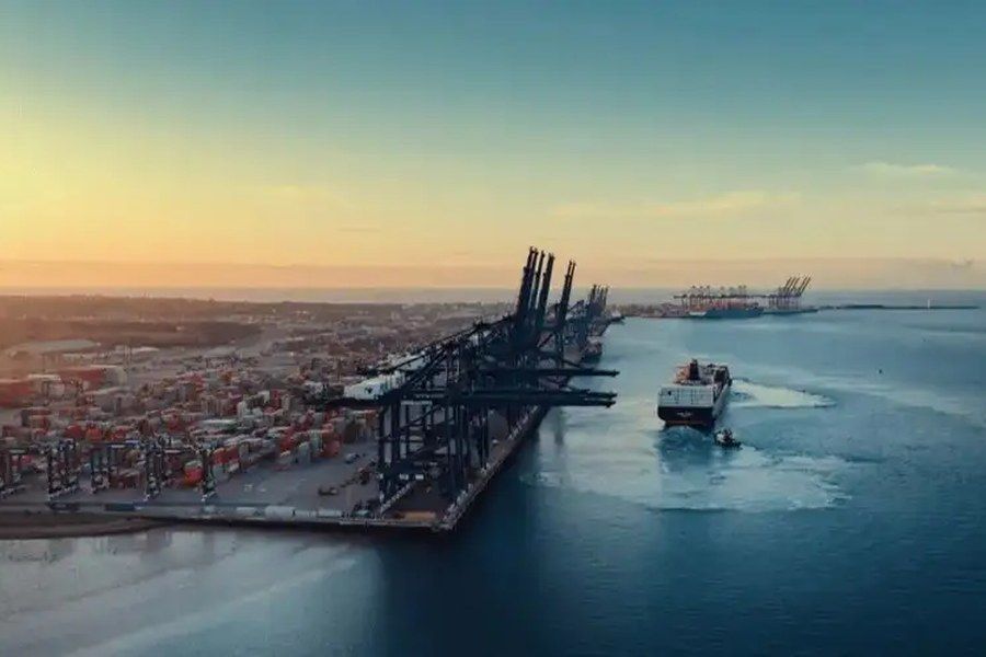 An aerial view of an Asian container terminal at sunset, with gantry cranes and a vessel under tow.