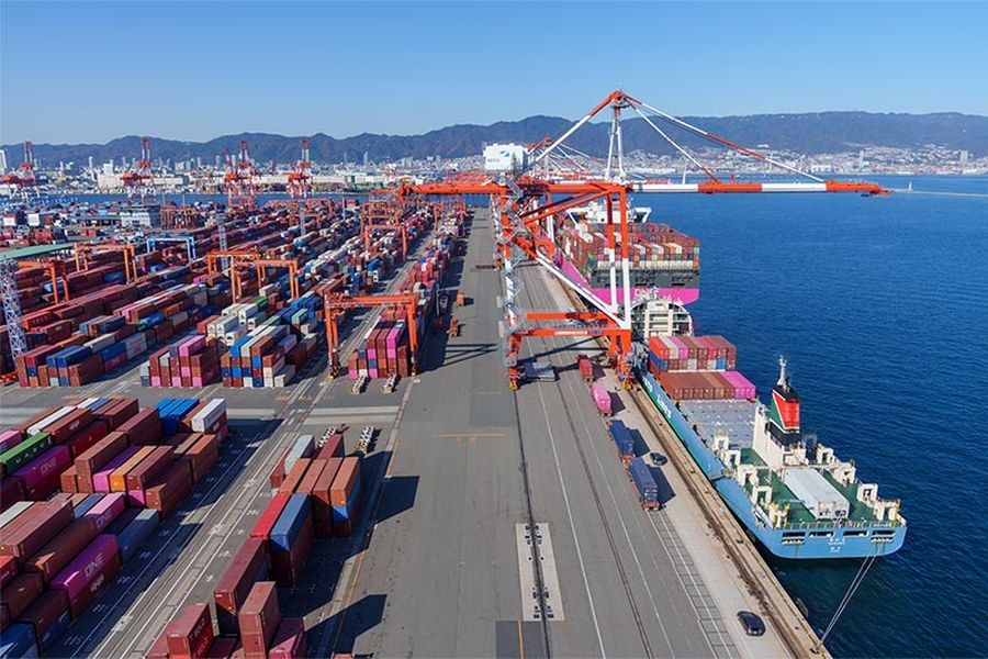 A container vessel working cargo alongside a Japanese terminal, with gantry cranes and stacked containers.